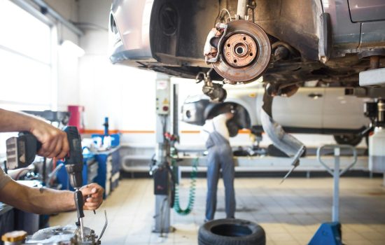 The car is lifted for repair on a lift in a car service station, a mechanic in overalls repairs